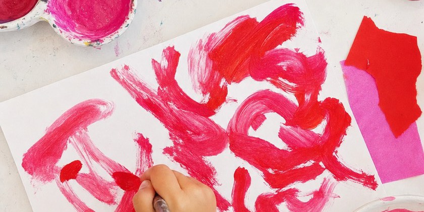 A child's hand painting red shapes over and over on white paper