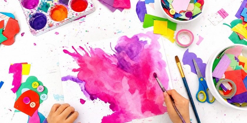 A child's hand painting pink and purple watercolour wet on wet