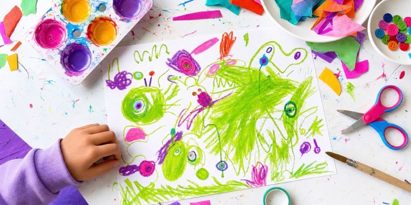 Hands making scribble creatures at a bright table