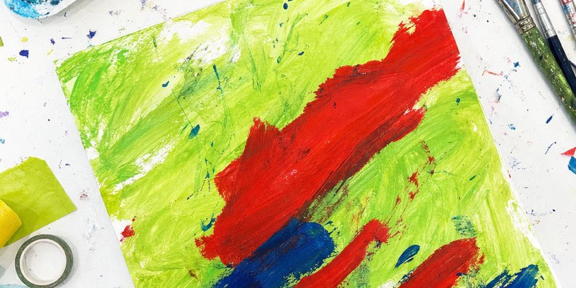 A child's hand making big bold strokes of red and blue paint over green