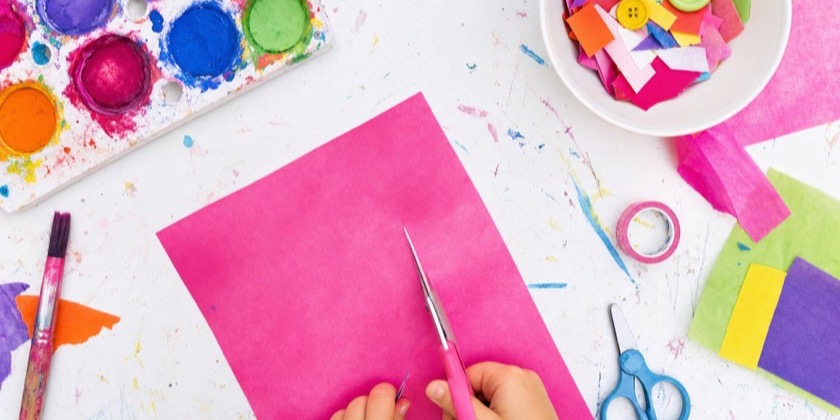 A child's hands cutting carefully along a line on pink paper
