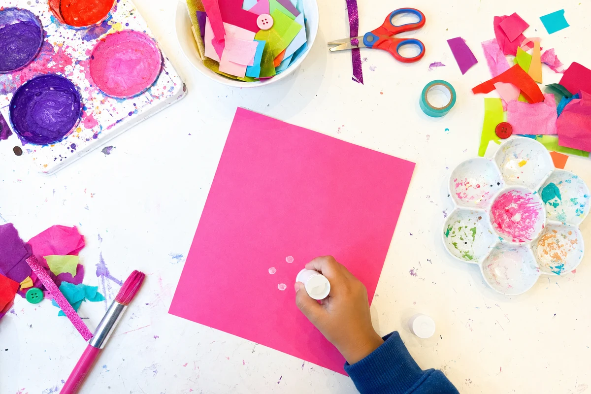 A hand dotting a glue stick on paper with the lid placed beside it