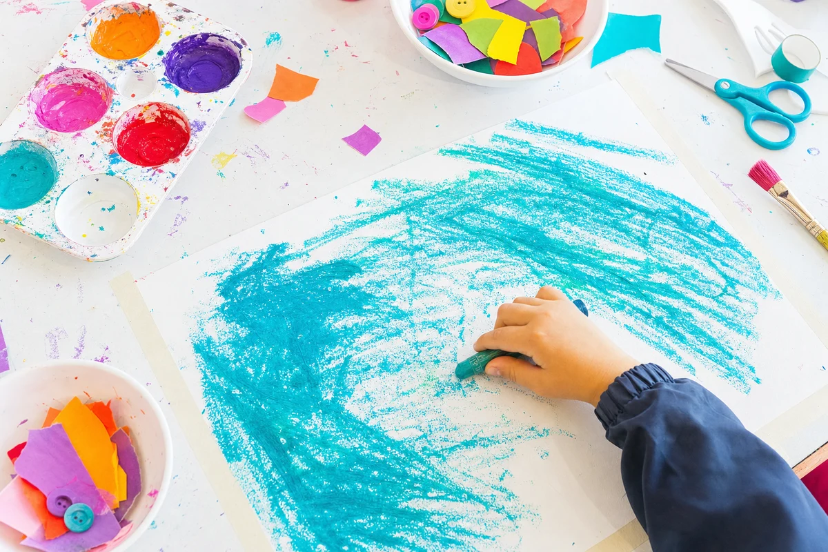 A hand dragging a crayon on its side across a big taped-down sheet
